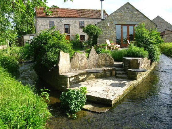 Eine aus Stein erbaute Struktur mit einer Steinsitzbank und einem Tisch an einem Kanal, umgeben von viel Grün.