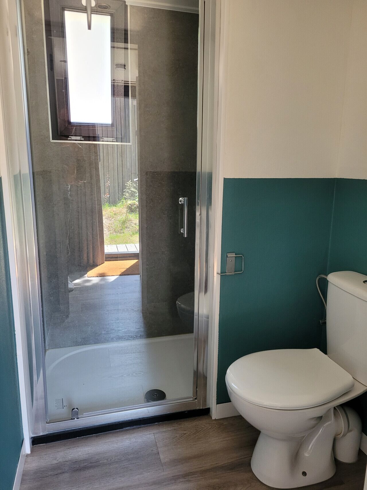 Ein Badezimmer mit Duschkabine aus Glas, einer weißen Toilette und einer türkisblauen Wand.