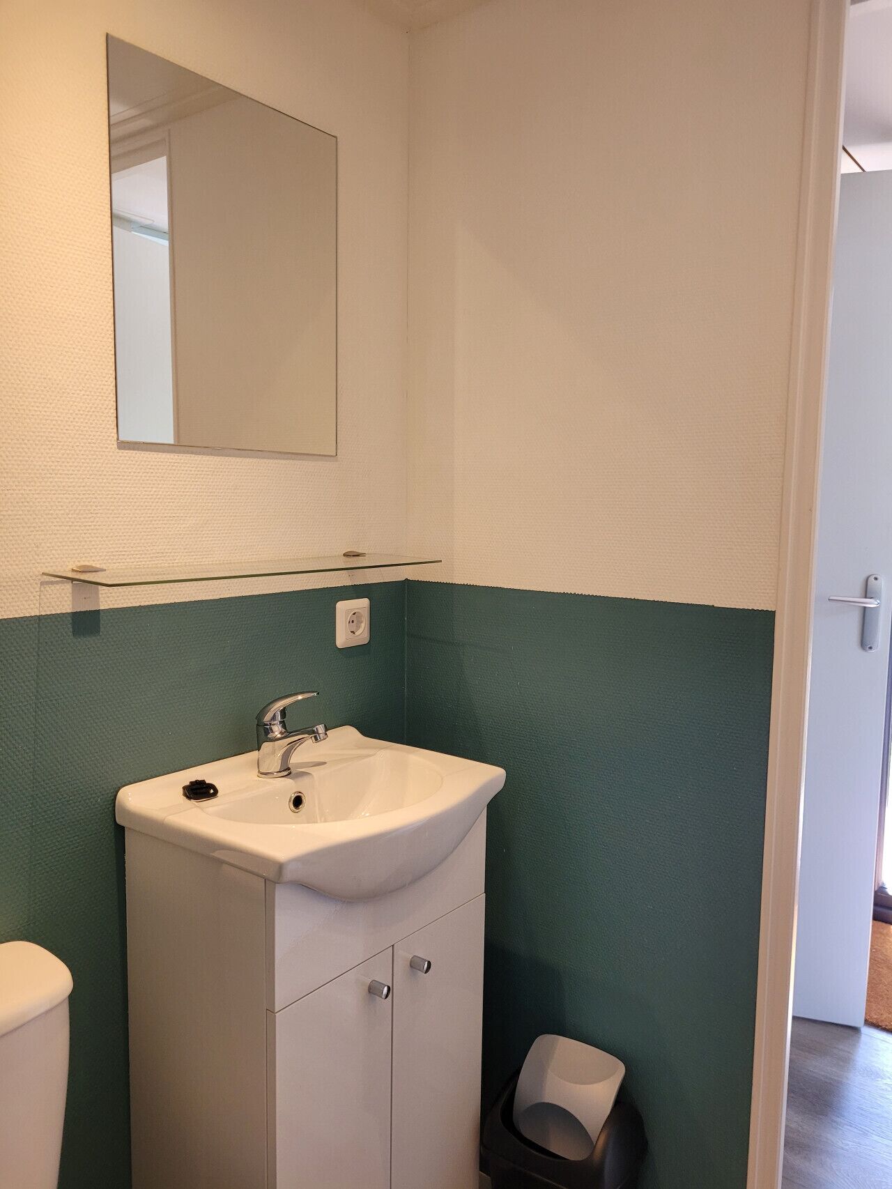 A bathroom with a white sink, a mirror above it, and a green wall.