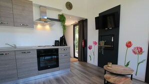 Cozinha moderna com forno embutido, cafeteira e uma planta no balcão. Possui um espaço de jantar com mesa redonda e duas cadeiras.