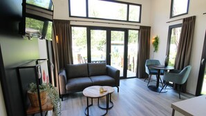Uma sala de estar moderna com um sofá, uma mesa de centro redonda, uma mesa de jantar com cadeiras e grandes janelas com cortinas.