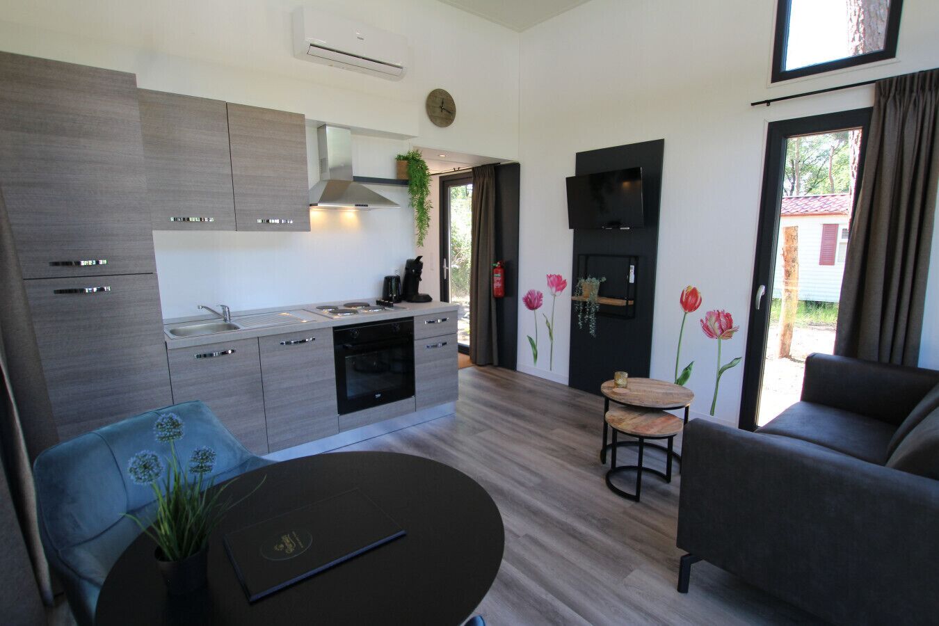 Uma cozinha moderna com forno e fogão embutidos, uma área de refeições com uma mesa redonda e uma sala de estar com sofá e televisão.