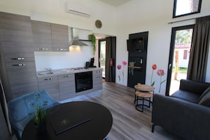 A modern kitchen with a built-in oven and stove, a dining area with a round table, and a living area with a sofa and a TV.