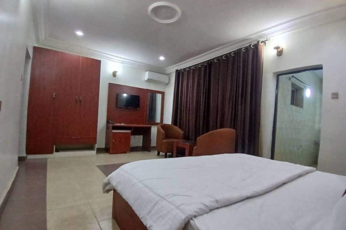A hotel room with a bed, a desk, two chairs, a TV, and a wardrobe.