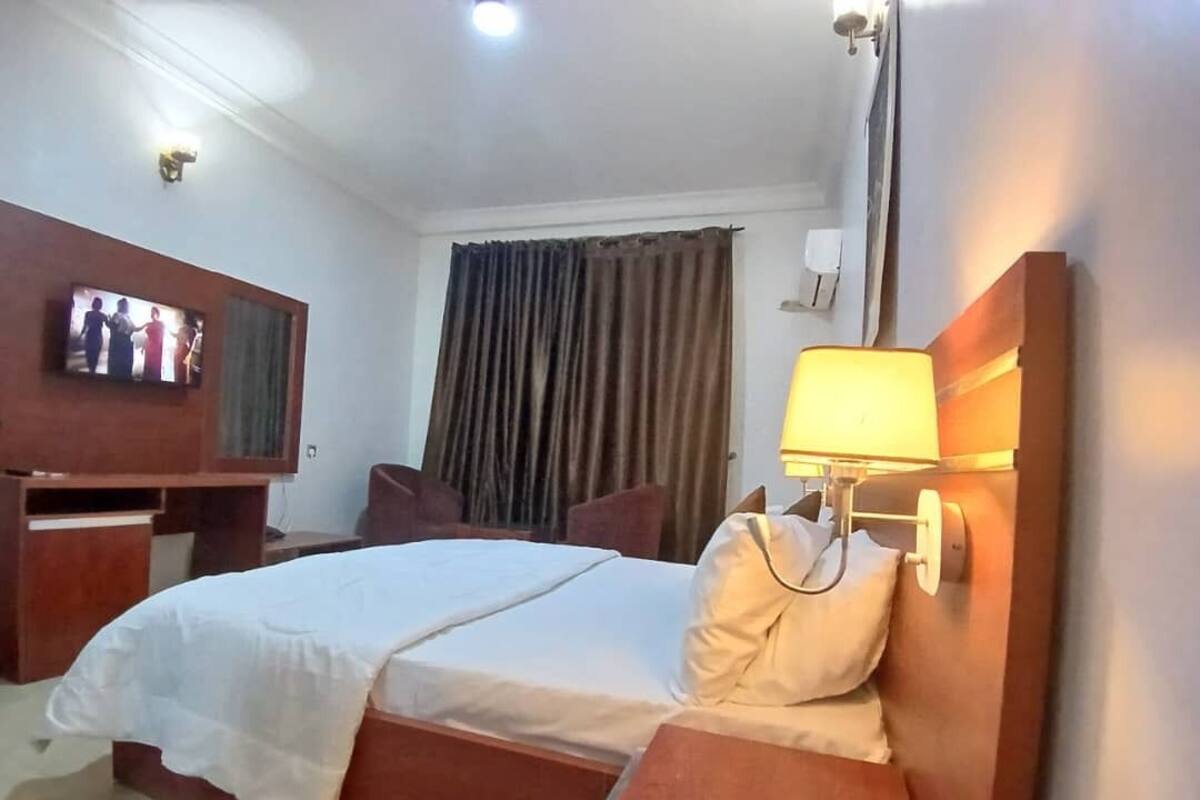 A hotel room with a bed, bedside table, lamp, TV, and curtains.