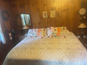 A wooden-paneled room with a bed, two wall-mounted lamps, and a mirror.