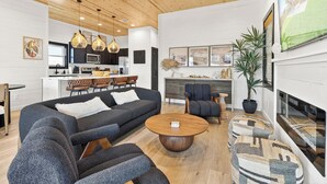 En moderne stue med sofa, stole, et sofabord og et spiseområde med et køkken i baggrunden.