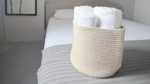 A bedroom with a bed, a woven basket with towels, and a framed picture of palm trees on the wall. - 2-bedroom apartment in tranquil Santafe de Antioquia with AC (Santafe de antioquia)