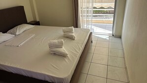 Una camera d'hotel con un letto, una finestra con tende e vista sull'esterno, e un pavimento piastrellato.