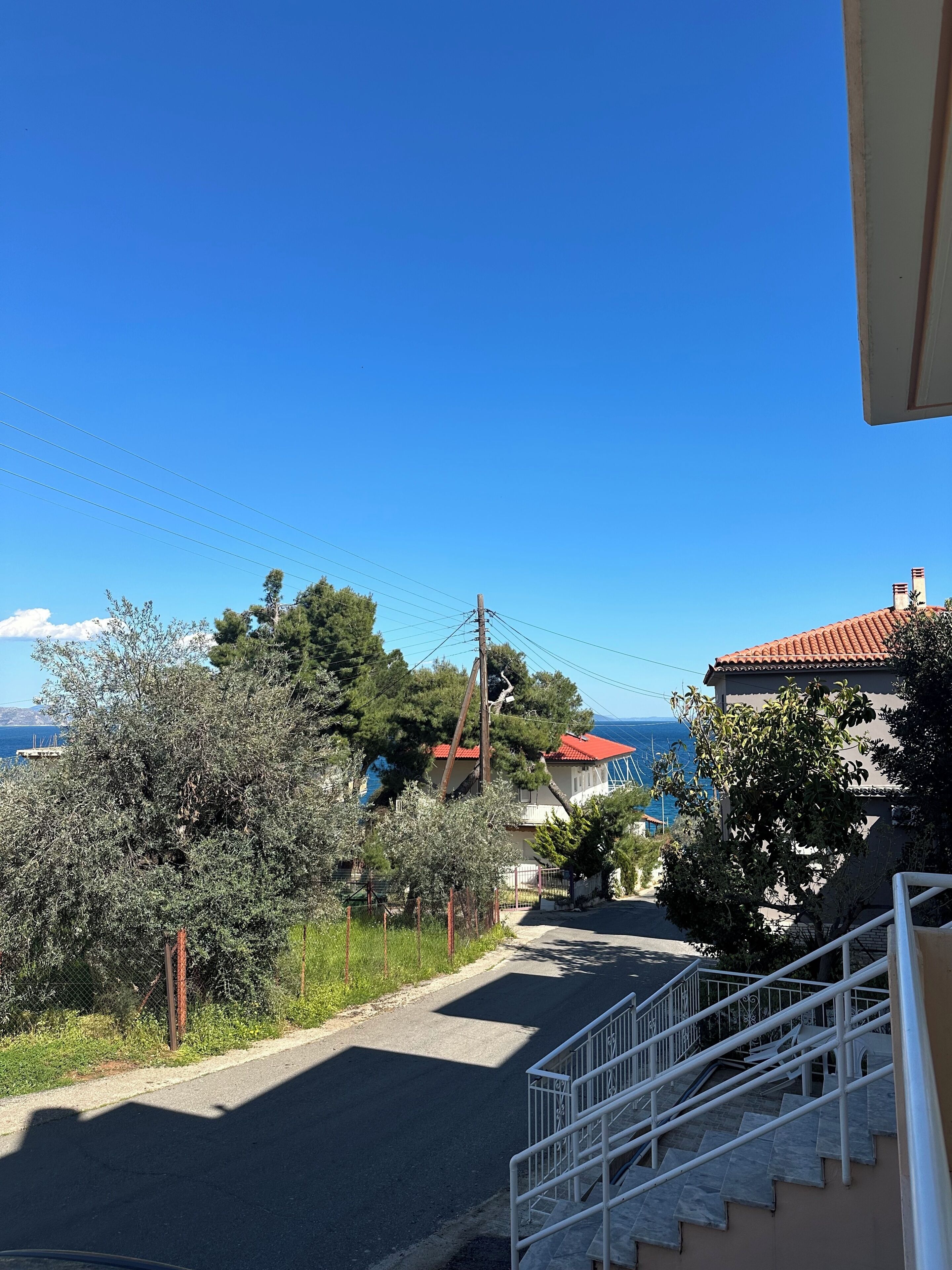 A residential street with a clear view of the sea, a staircase, and a fence.