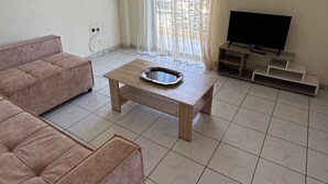 Un soggiorno con un divano, un tavolino, una televisione e una finestra con tende.