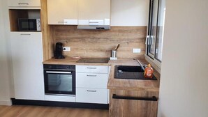 A modern kitchen with a built-in oven, microwave, and a wooden countertop. - L'Appartement Soleil - Clermont Centre (Clermont-Ferrand)