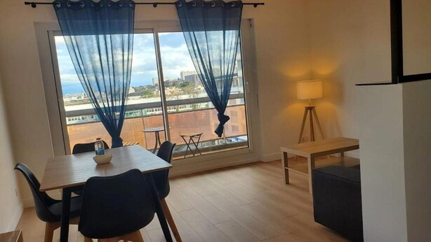 A room with a dining table, chairs, a lamp, a bench, and a view through a window with curtains. - L'Appartement Soleil - Clermont Centre (Clermont-Ferrand)