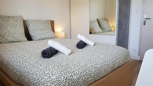 A neatly made bed with patterned bedding, a bedside lamp, and a mirror reflecting the bed. - L'Appartement Soleil - Clermont Centre (Clermont-Ferrand)