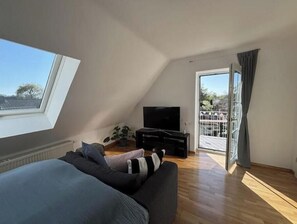 Ein Schlafzimmer mit großem Fenster, Fernseher, Sofa und Balkon.