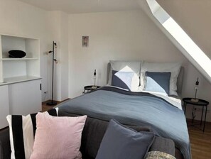 Ein Schlafzimmer mit Bett, Kissen, einem Nachttisch, einem Regal und einem Bild an der Wand.