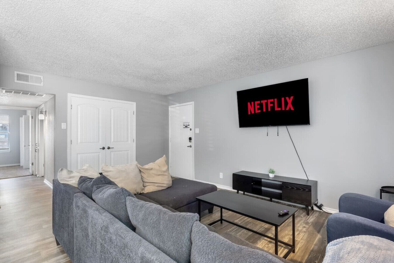 A modern living room with a grey sofa, a black coffee table, and a TV mounted on the wall displaying 'NETFLIX'.