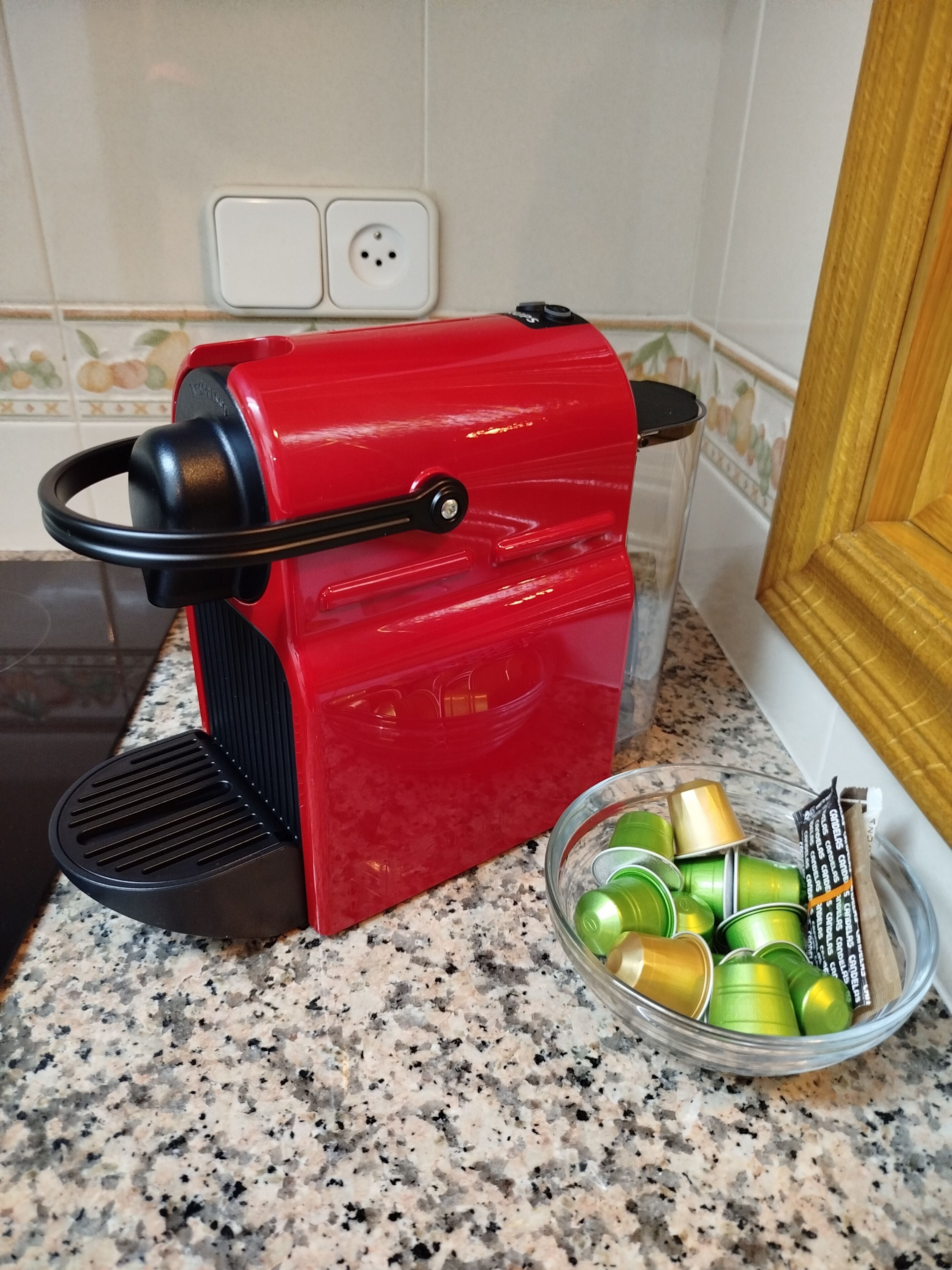 Een rode koffiezetapparaat op een granieten aanrecht, met een kom groene en gouden blikken in de buurt.