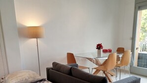 Una habitación de hotel moderna con una cama, un sofá, una mesa de comedor con sillas, una lámpara y vistas al exterior.