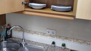Una cocina con encimera de granito, pileta de acero inoxidable y estantes de madera con tazas y cristalería.