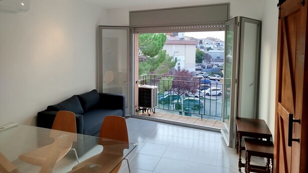 Una sala moderna con una mesa de vidrio, un sofá y un balcón con vista a coches estacionados y edificios.