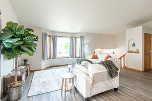Ein Schlafzimmer mit Bett, Nachttisch, Lampe, einer großen Pflanze und Blick ins Freie.