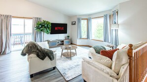 Een woonkamer met een bank, fauteuil, salontafel en een aan de muur bevestigde televisie.