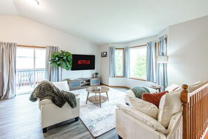 Ein Wohnzimmer mit Sofa, Sesseln, Couchtisch und einem an der Wand befestigten Fernseher.