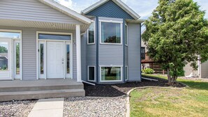 Een tweelaags huis met een veranda, een garage en een boom in de voortuin.