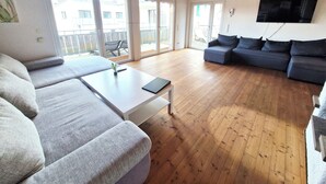 Een ruime woonkamer met een bank, een salontafel en een aan de muur bevestigde televisie.