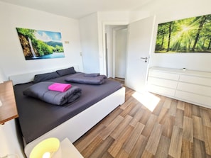 A bedroom with a bed, a desk, a chair, a wardrobe, and two wall-mounted paintings.