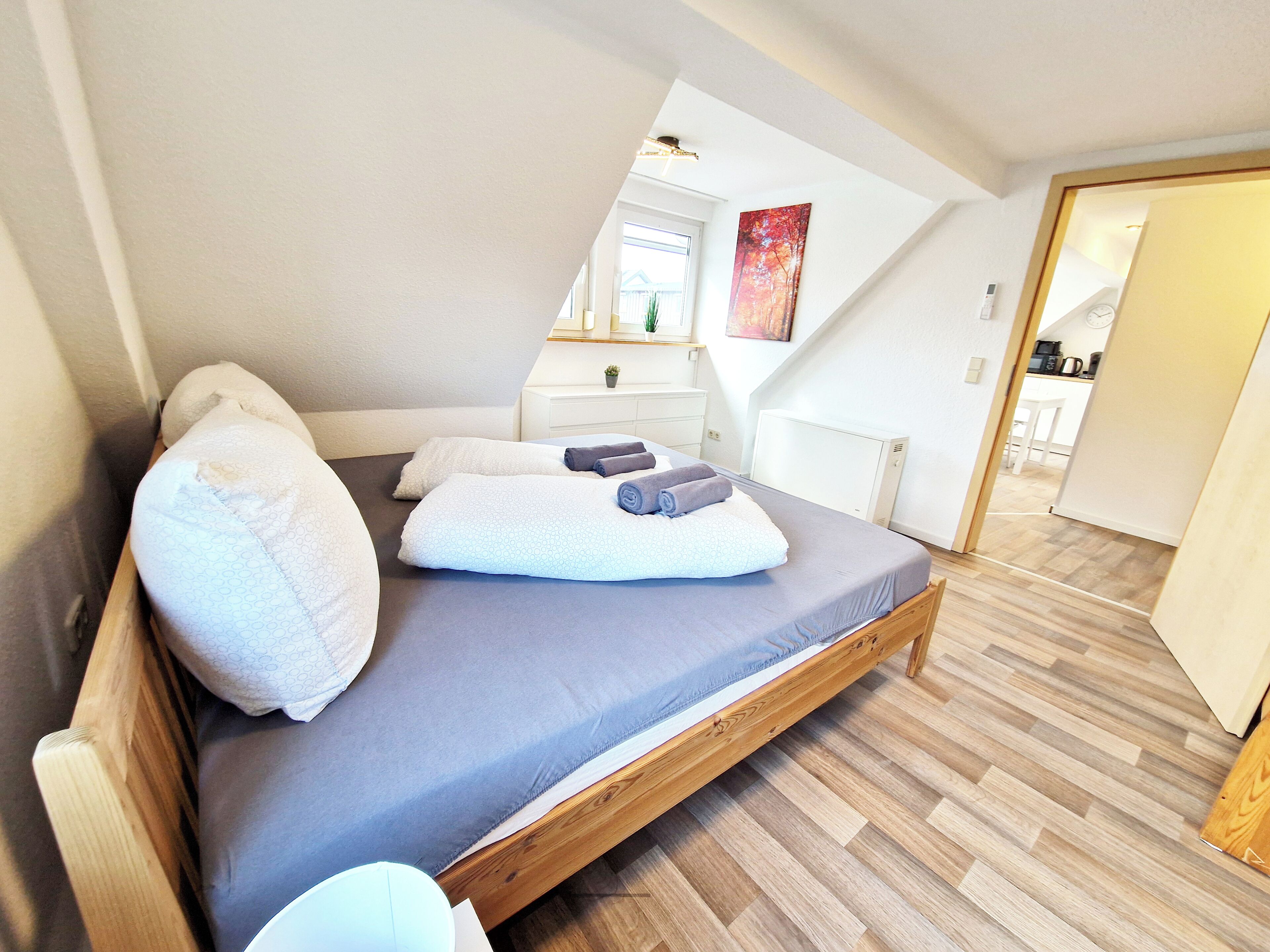 A bedroom with a wooden bed, a gray mattress, and white pillows.