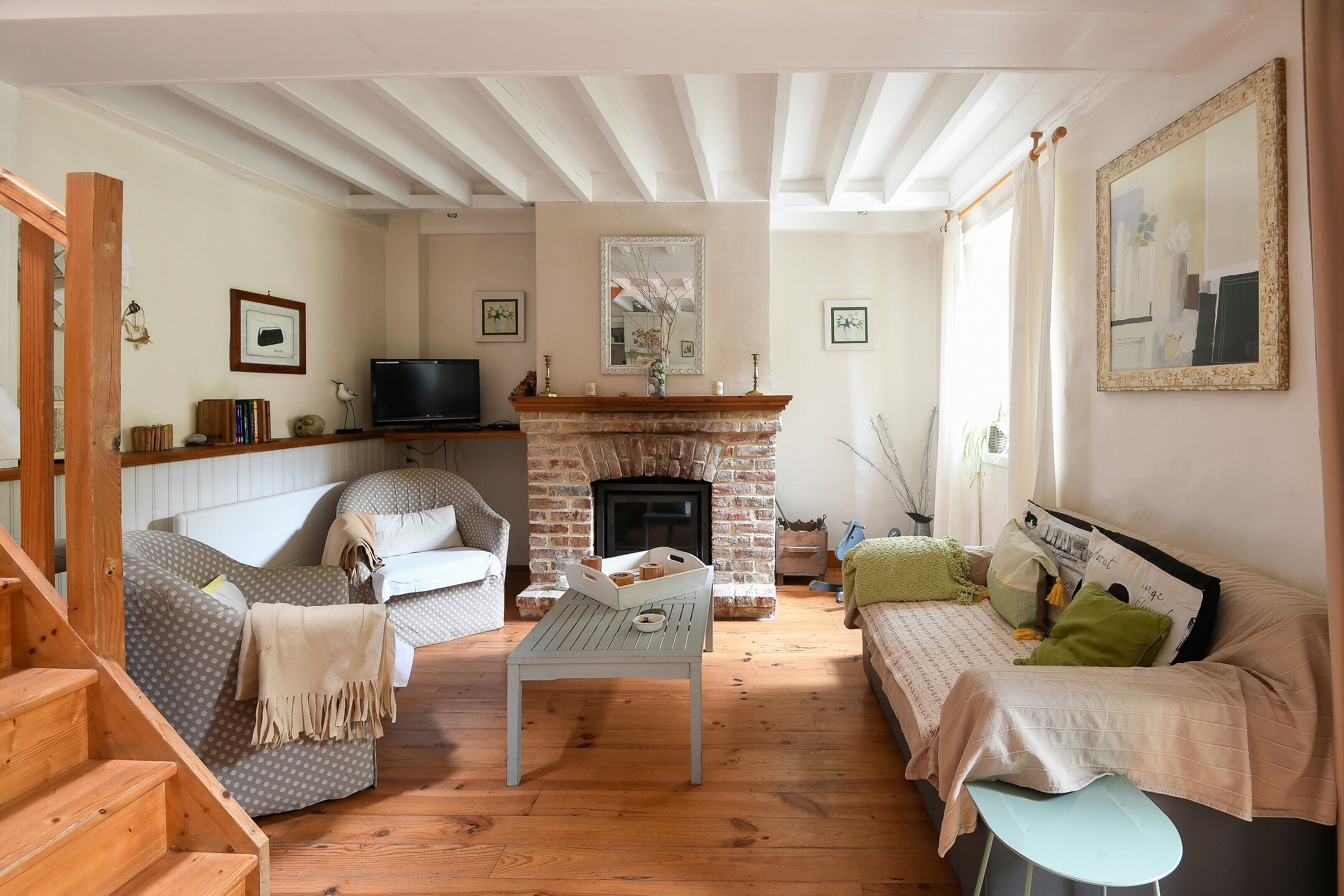 A living room with a fireplace, wooden flooring, a sofa, a coffee table, and a television.