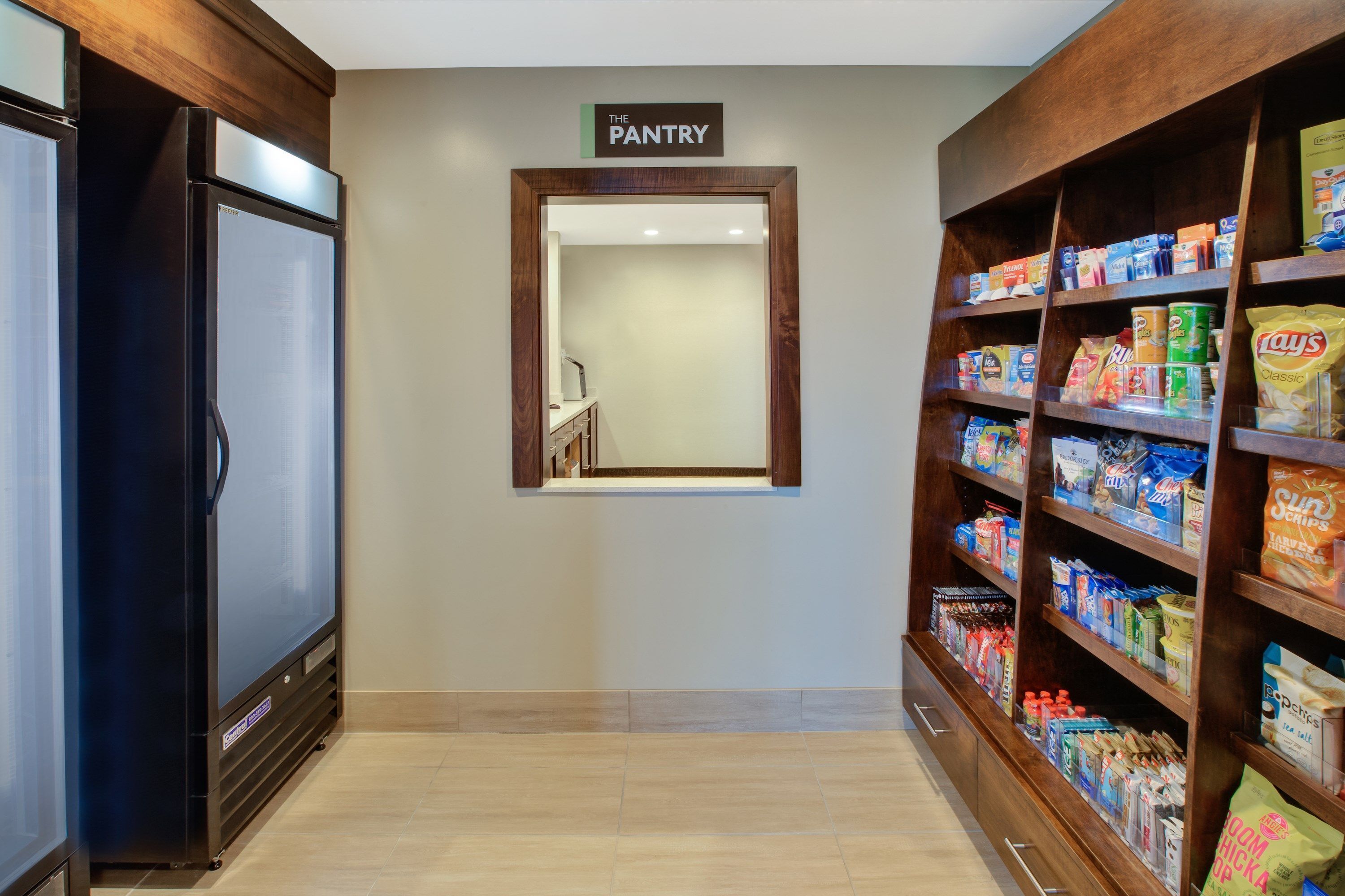 A pantry area with shelves stocked with snacks and beverages, a refrigerator, and a sign indicating the location.