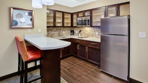 Una cocina con un refrigerador de acero inoxidable, un microondas, un lavamanos y una zona de comedor con una silla.
