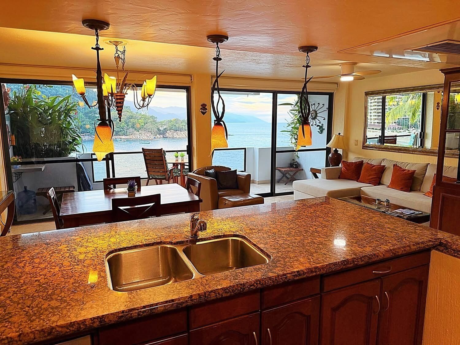 A kitchen with granite countertops, stainless steel sinks, and pendant lights.