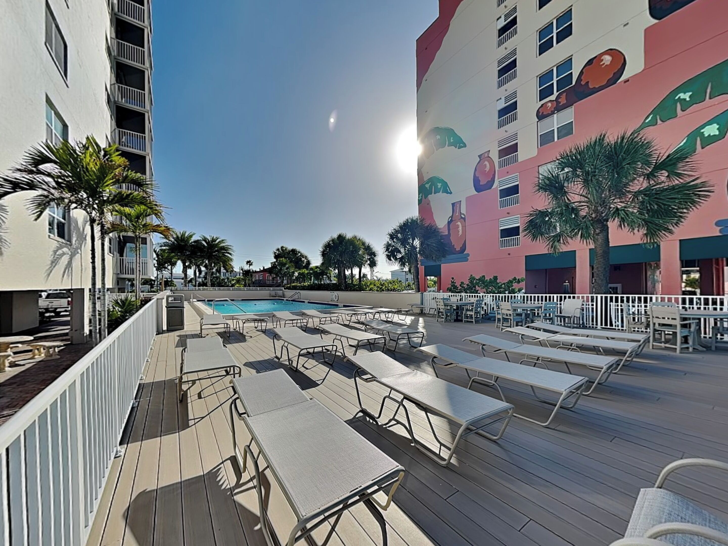 Un espace aménagé au bord de la piscine, avec des chaises longues et une piscine, le tout entouré d’immeubles dotés de balcons et de palmiers.