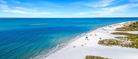 Ein Strand mit klarem, blauem Wasser, weißem Sand und einigen Personen.
