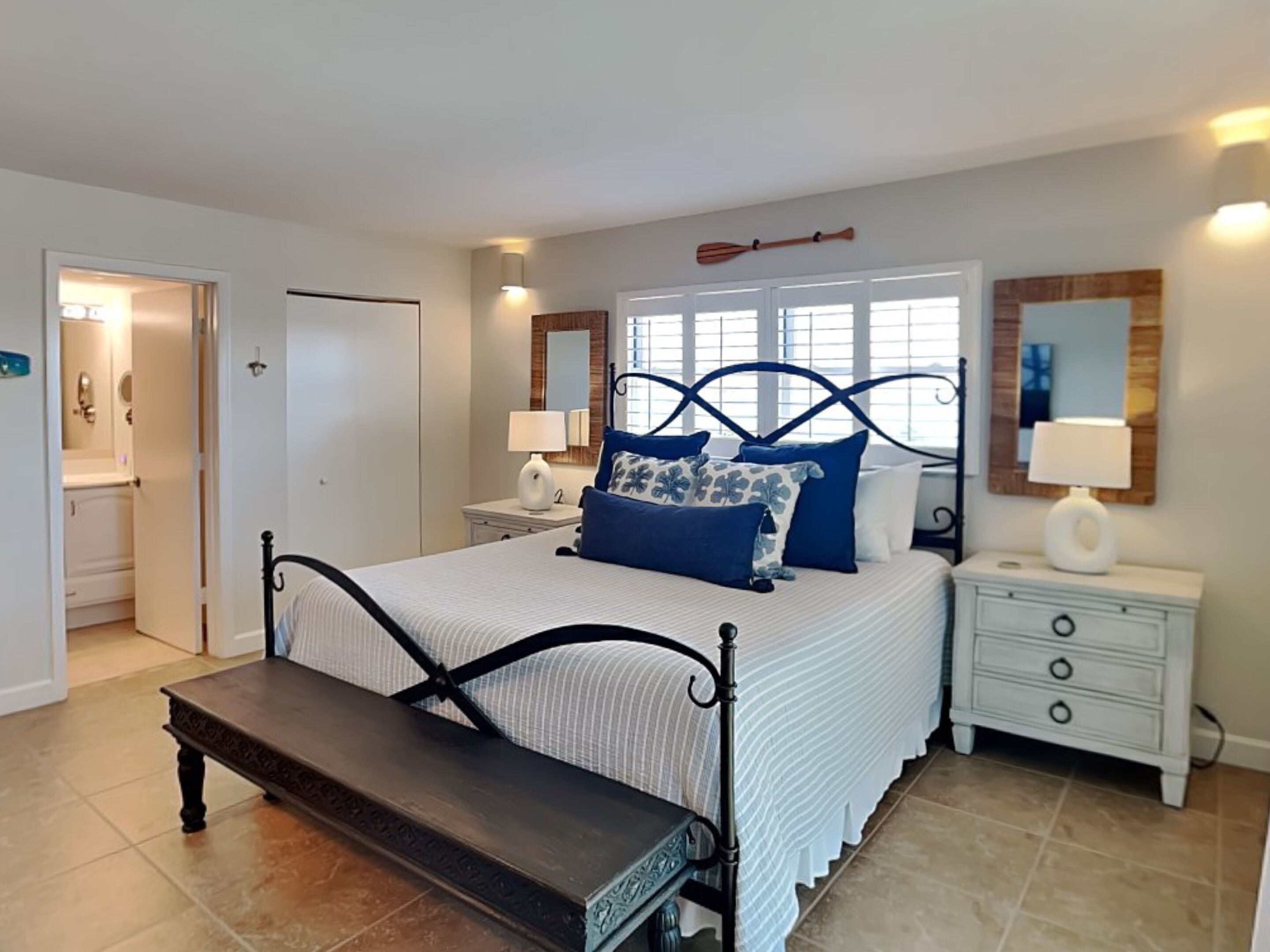 A bedroom with a bed, bedside tables, a bench, and a door leading to a bathroom.