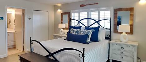 A bedroom with a bed, bedside tables, a bench, and a door leading to a bathroom.