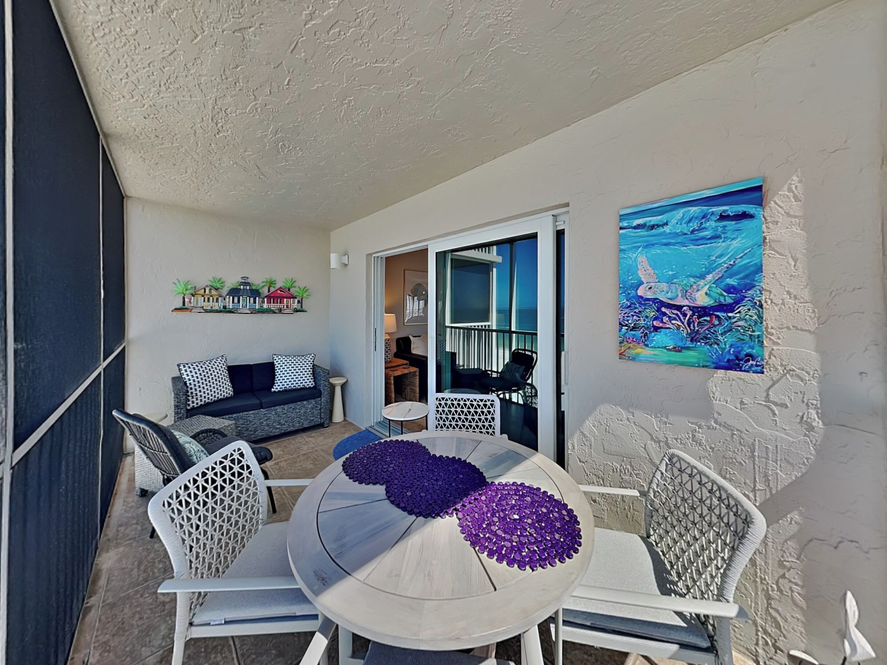 A balcony with a round table, white chairs, a sofa, and a painting.