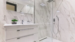A modern bathroom with a marble sink, a small potted plant, a mirror, and a glass-enclosed shower.