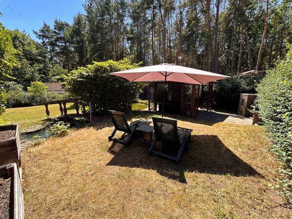 A patio with a table and chairs, a pergola with a red umbrella, and a wooden fence.