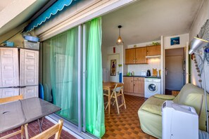 A compact kitchen with a washing machine, a dining table, and a sofa. - Studio "Cabine Bord De Mer" with Shared Pool, Balcony, and Air Conditioning (Le Grau-du-Roi)