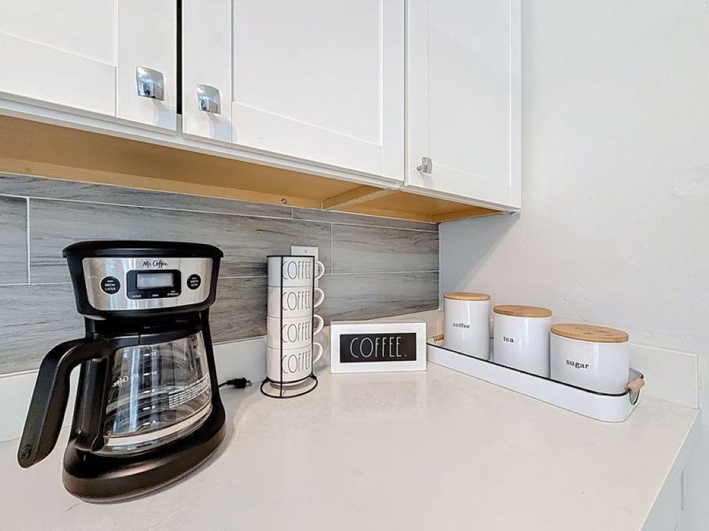 A kitchen with a coffee maker, a coffee station, and containers labeled coffee, tea, and sugar.