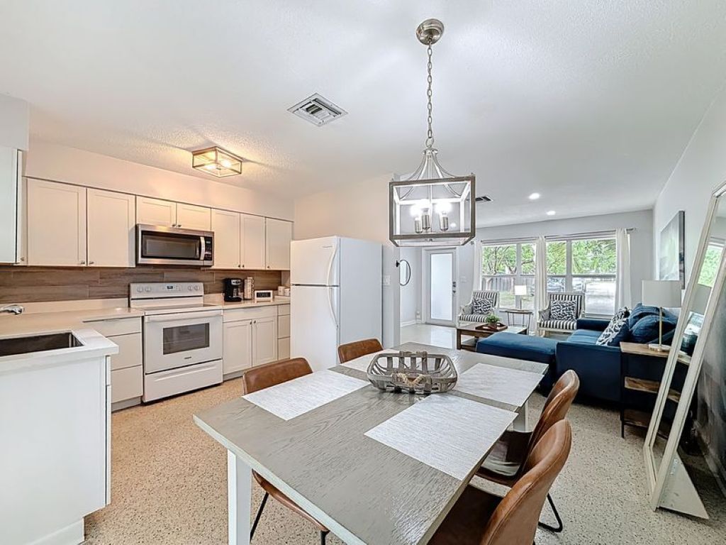 A modern kitchen with white cabinets, a microwave, and a dining area with a table and chairs.