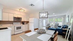 A modern kitchen with white cabinets, a microwave, and a dining area with a table and chairs. - Serene 2-bedroom house minutes to Beach Restaurants (Pompano Beach)