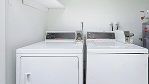 A laundry room with two white washers and dryers, a wall-mounted shelf, and a water heater. - Serene 2-bedroom house minutes to Beach Restaurants (Pompano Beach)
