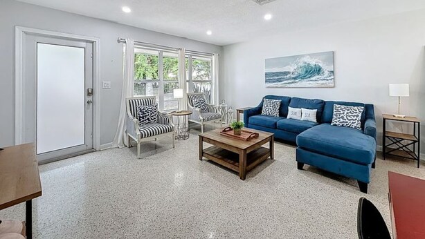 A living room with a blue sofa, striped chairs, a coffee table, and a painting of a wave. - Serene 2-bedroom house minutes to Beach Restaurants (Pompano Beach)