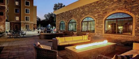 An outdoor patio with a fire feature, wicker furniture, and a stone wall.